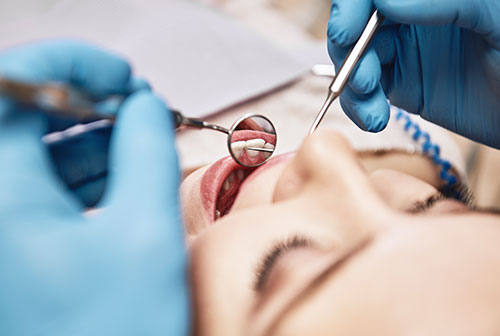 A dental professional performing oral surgery, with a patient s mouth open and a surgical instrument in use.